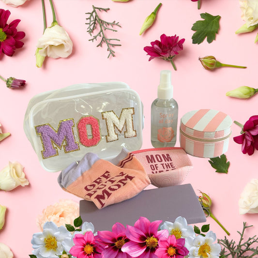 Self care gift set for moms featuring a clear MOM bag, beauty accessories, and wellness products surrounded by pink flowers.