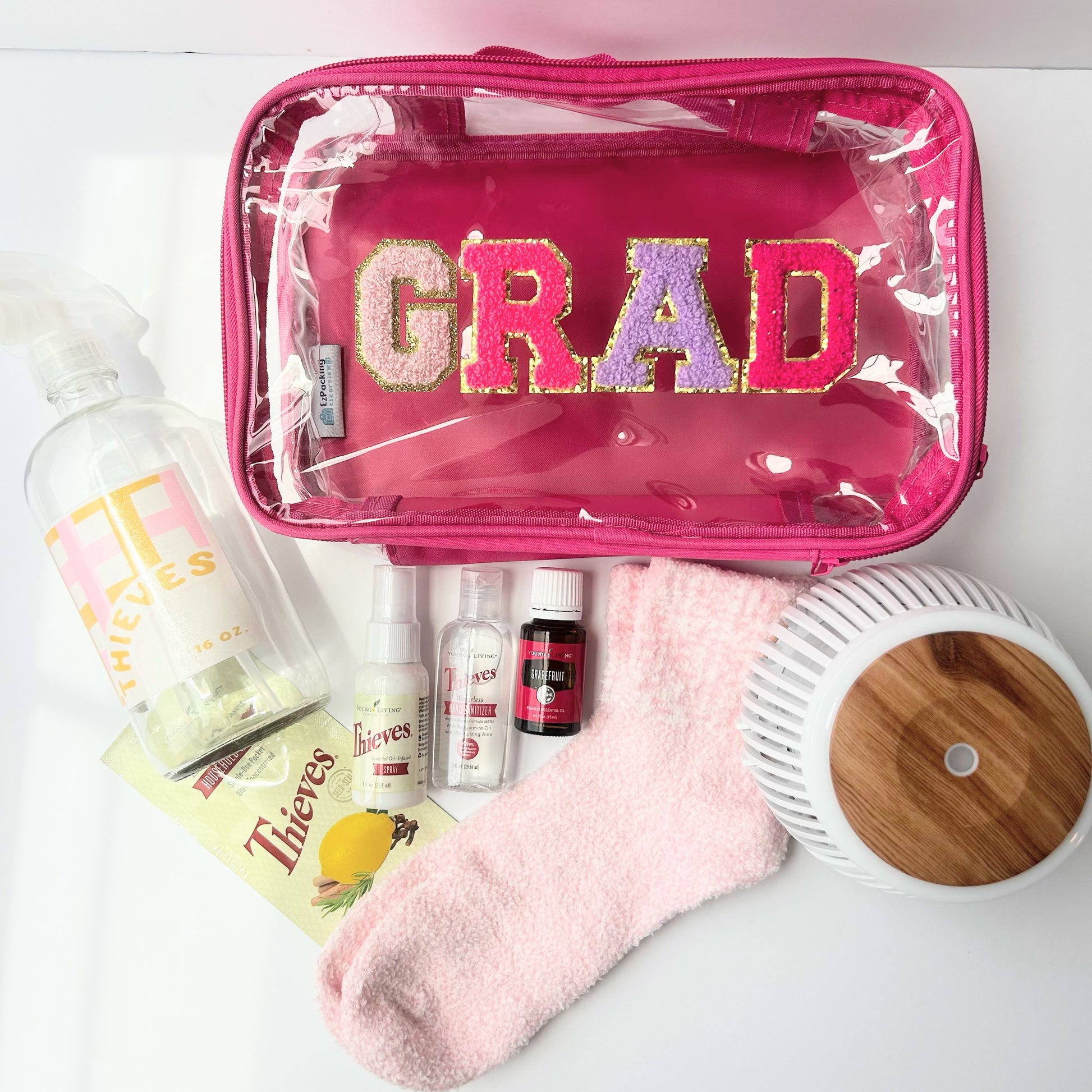 Self-care graduation gift bundle with diffuser, Thieves wellness products, grapefruit essential oil, cozy socks, and reusable grad travel pouch for college students.