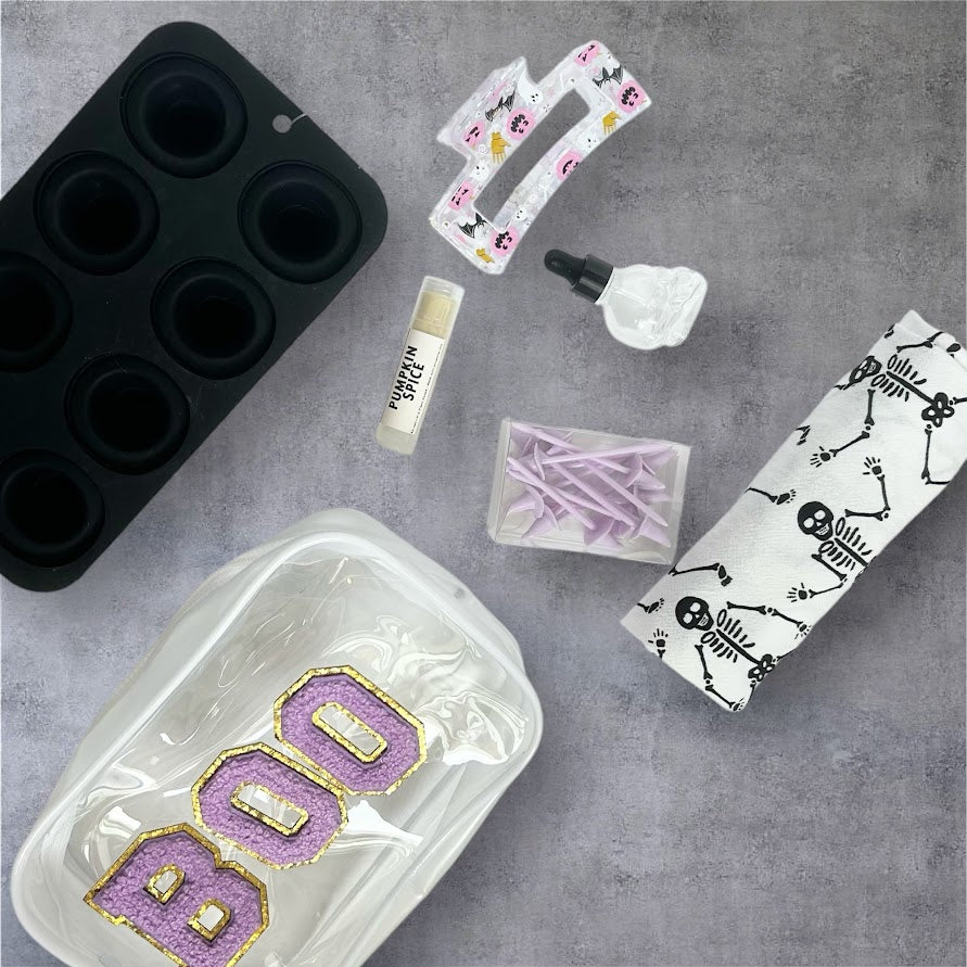 Purple BOO Halloween Wellness Gift Bundle with skeleton dish towel, pumpkin spice lip balm, skull bottle, ice mold, hair clip and seasonal accessories.