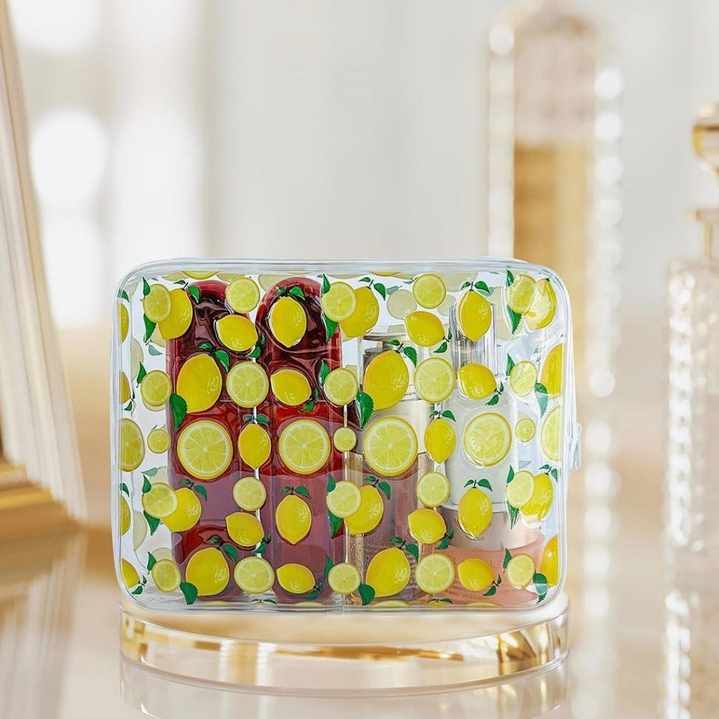 Lemon-print clear cosmetic bag filled with skincare and beauty products on a vanity table.
