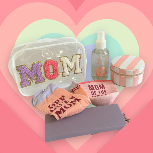 Mom wellness gift bundle featuring a clear MOM cosmetic bag, self-care accessories, socks, and beauty essentials on a pastel rainbow heart background.