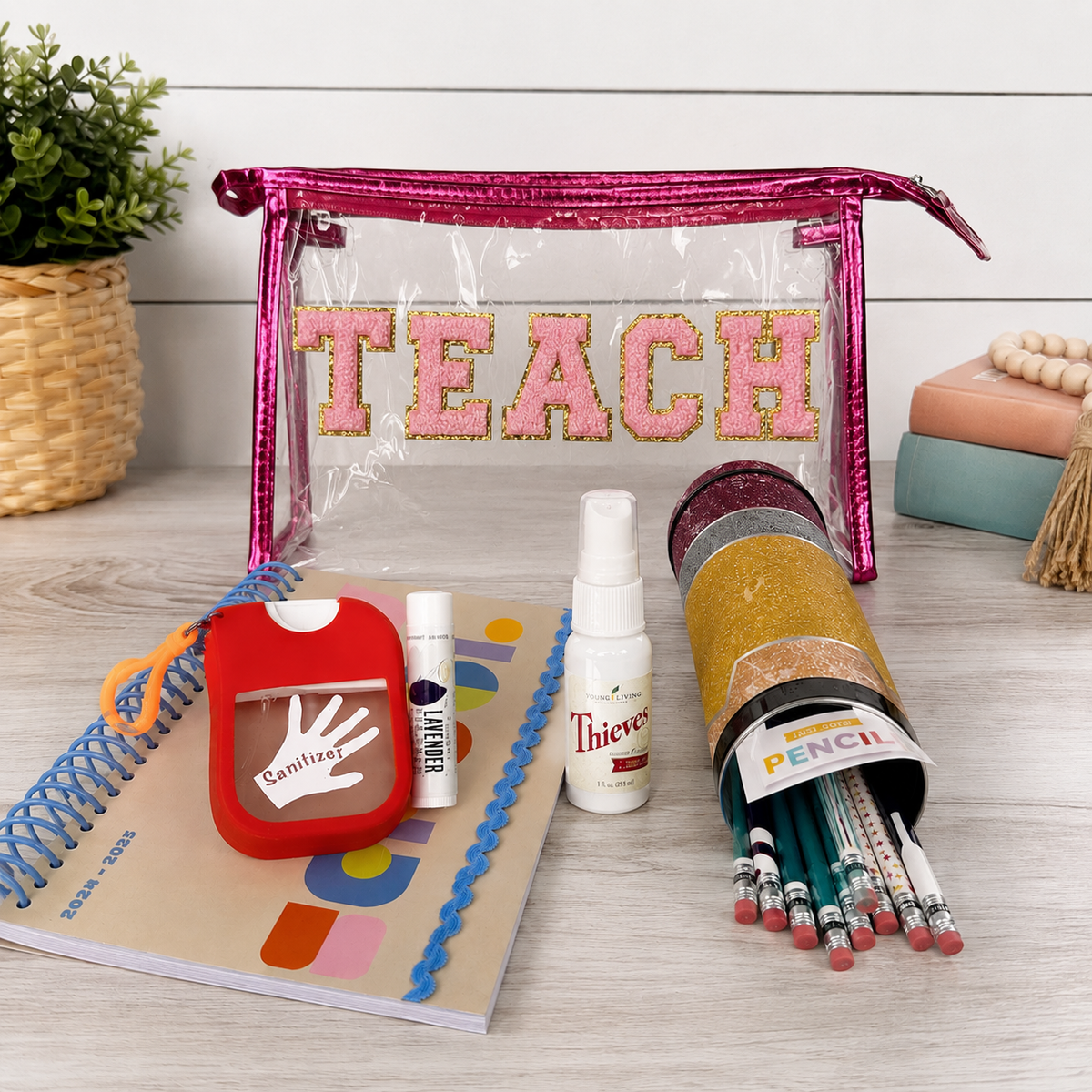 Teacher wellness gift bundle with clear TEACH pouch, colorful planner, pencil set, sanitizer holder, lip balm, and Thieves spray arranged on a bright tabletop.